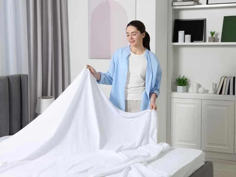 Persona cambiando las sábanas de una cama bien iluminada en una habitación ordenada