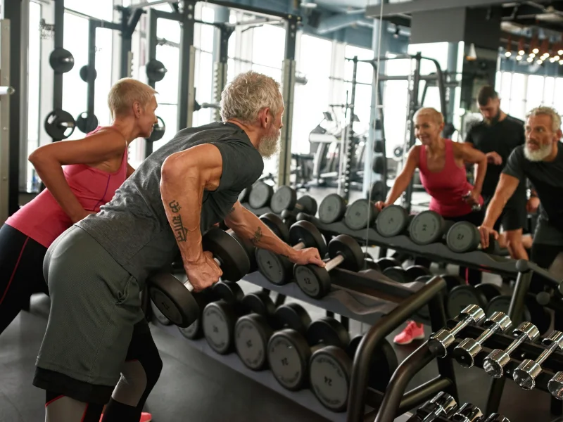 adultos-mayores-entrenando-fuerza-con-mancuernas-gimnasio