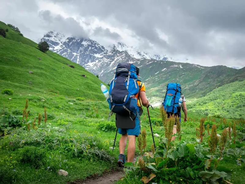 Senderistas caminando por un prado verde en los Pirineos con montañas escarpadas de fondo