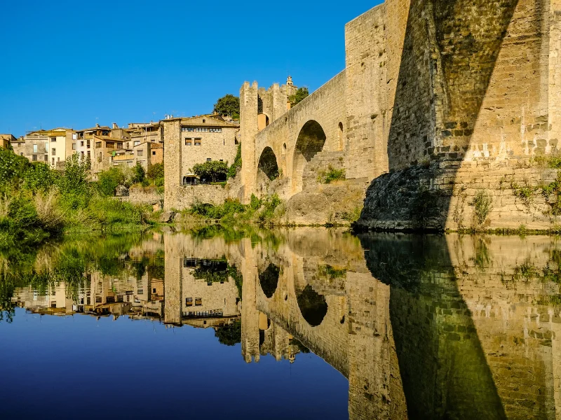 Puente románico de Besalú reflejado sobre el río Fluvià en una mañana soleada