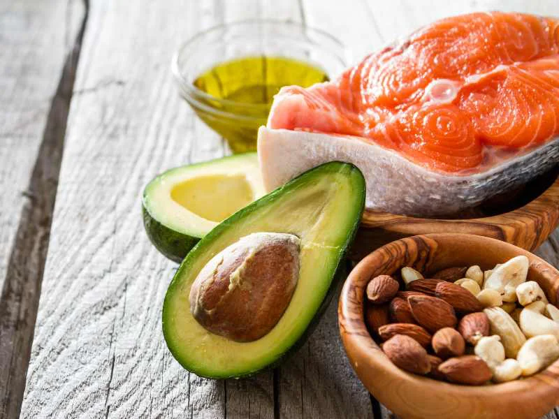 Selección de alimentos saludables como salmón, aguacate, nueces y frutos secos sobre una mesa de madera
