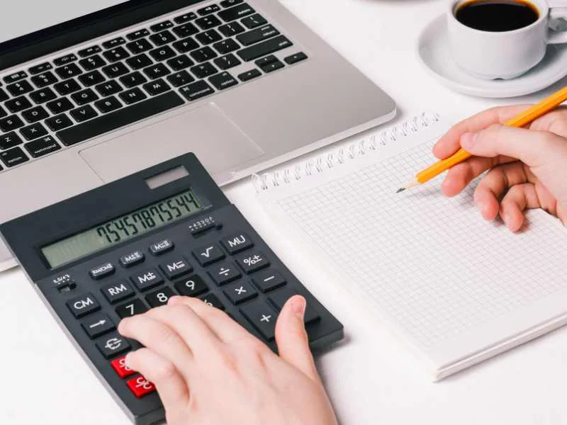 Una persona organizando su presupuesto mensual con una calculadora y una libreta sobre un escritorio