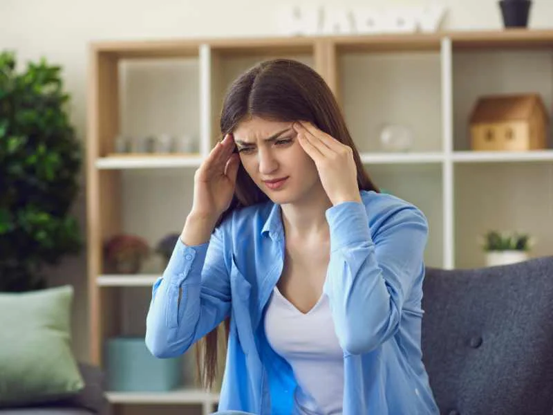 Persona con expresión de dolor de cabeza frotándose las sienes en un ambiente silencioso