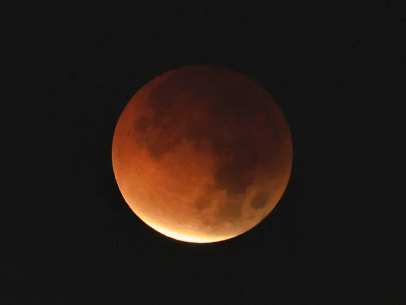 La Luna en fase de eclipse parcial mostrando una sombra oscura y tonos anaranjados sobre su superficie|Foto: EFE 