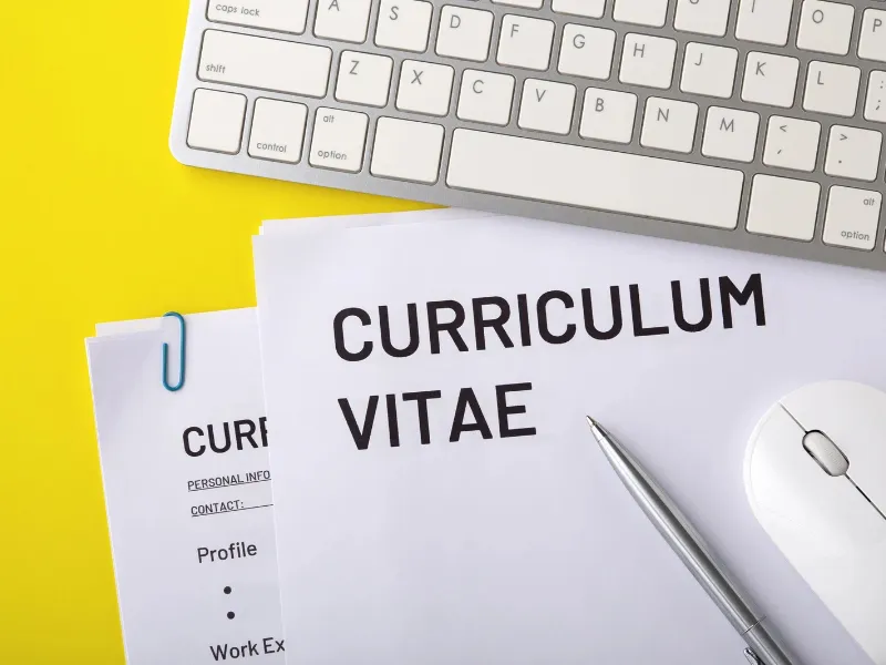 Currículum vitae impreso sobre un escritorio junto a un teclado y una pantalla de ordenador  Currículum junto a teclado y pantalla, listo para actualizar

