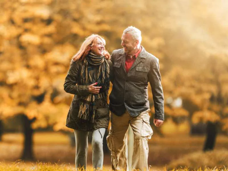 Pareja madura sonriendo mientras caminan al aire libre en un parque durante una mañana soleada