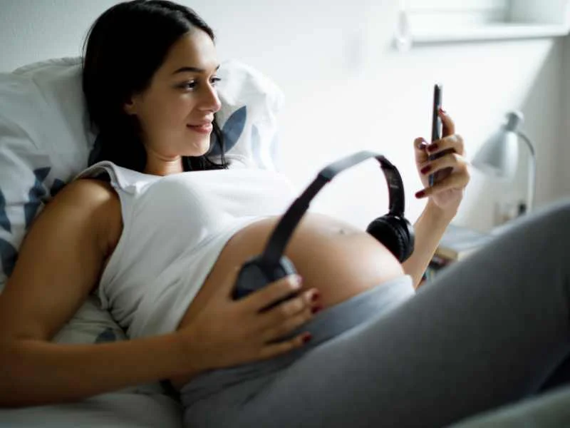 Mujer embarazada sonriendo mientras sostiene sus manos sobre el vientre con auriculares colocados