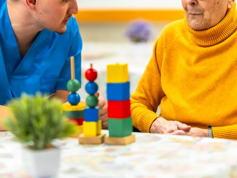 Una persona mayor realizando ejercicios de estimulación cognitiva junto a un profesional de la salud