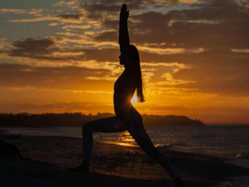 Persona practicando la postura del guerrero en yoga al aire libre durante el amanecer