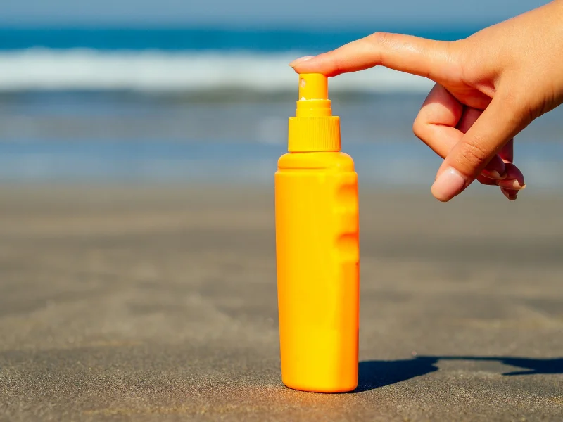 Frasco de protector solar sobre la arena frente al mar representando la evolución de la fotoprotección dermatológica