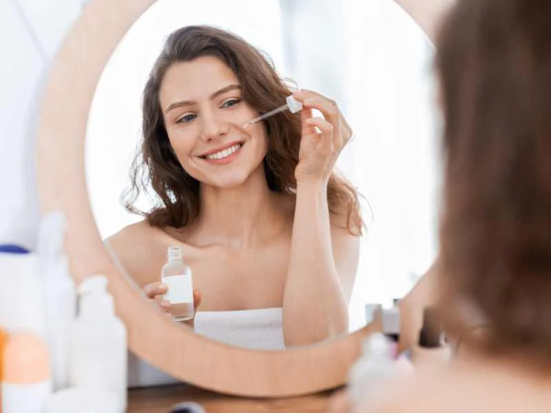 Mujer aplicando un sérum facial hidratante frente al espejo en un espacio bien iluminado