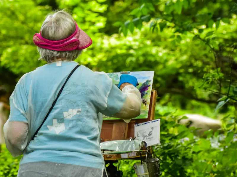 Persona adulta pintando un lienzo al aire libre rodeada de naturaleza