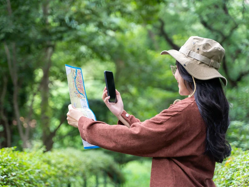 Persona planificando un viaje con un smartphone frente a un paisaje natural sostenible