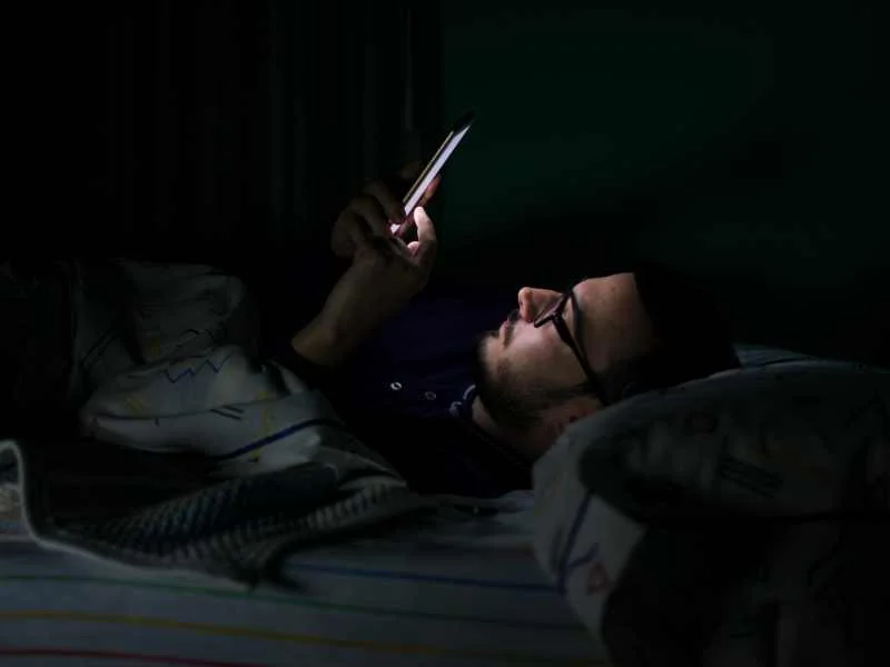 Persona mirando la pantalla encendida de un teléfono inteligente en una habitación a oscuras
