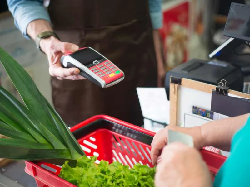 Tarjeta electrónica de compra sobre un mostrador de supermercado junto a alimentos frescos